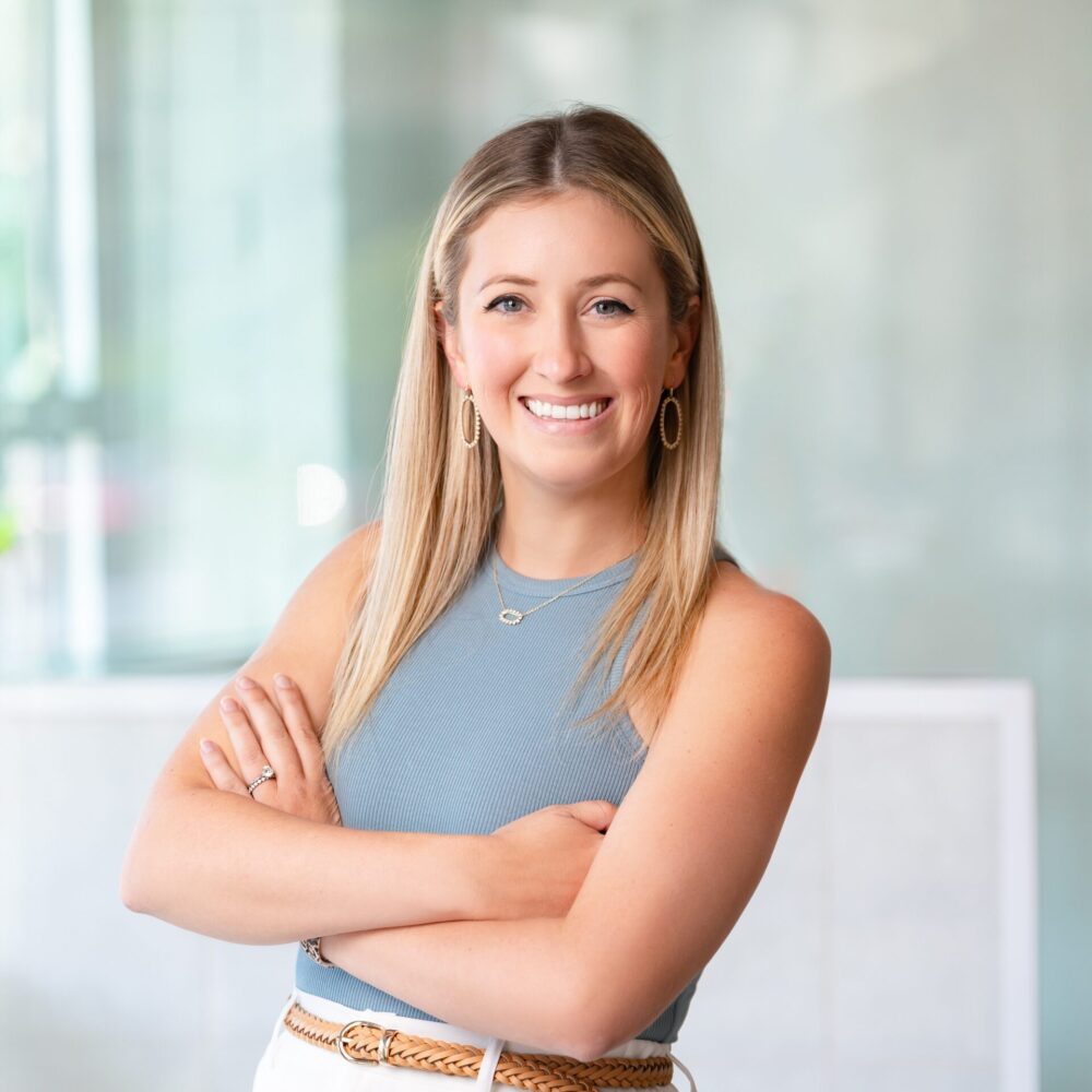 a headshot of a woman named Darian who has blonde hair and is wearing a blue tank top and white pants