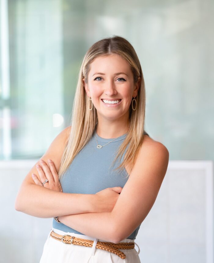 a headshot of a woman named Darian who has blonde hair and is wearing a blue tank top and white pants