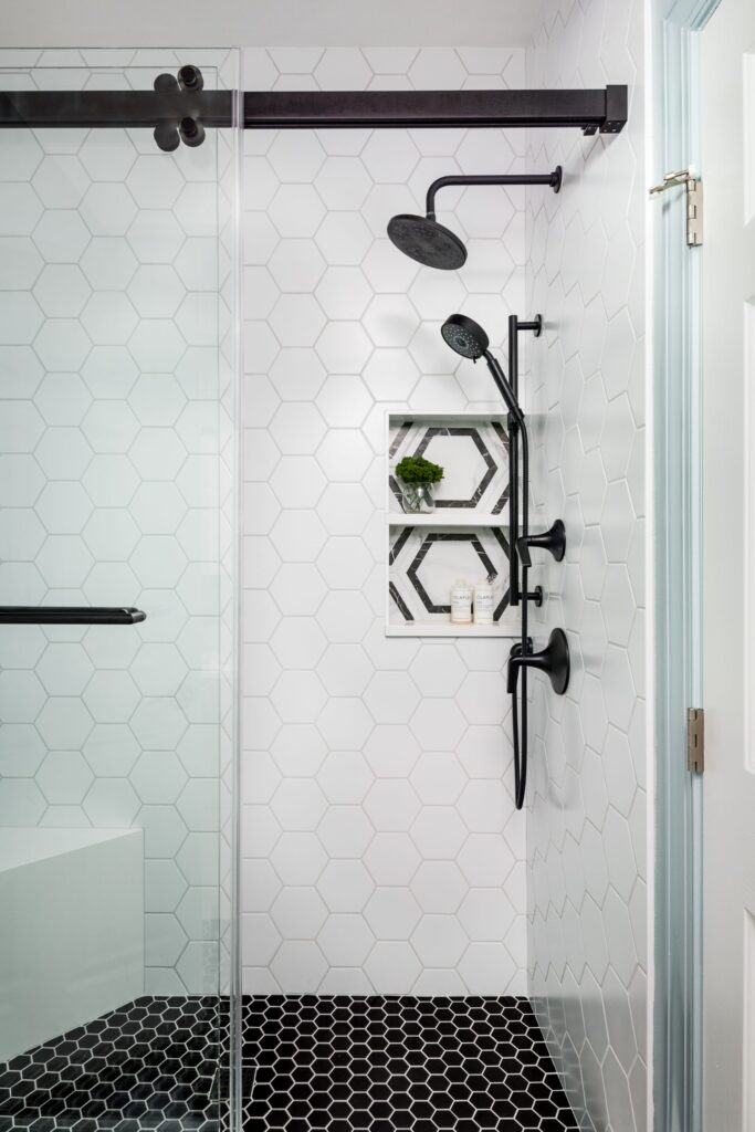 White tiled shower with white and black hexagon design and black hardware.