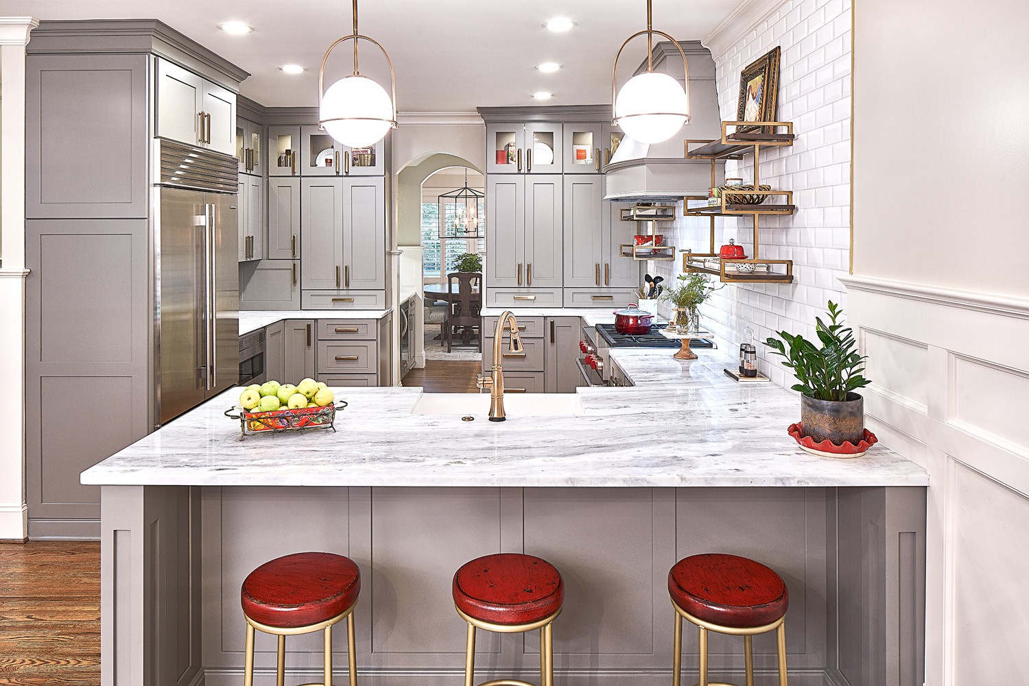 White and gray marble countertops contrast with the dovetail gray cabinetry. Red stools and accessories offer a pop of color.