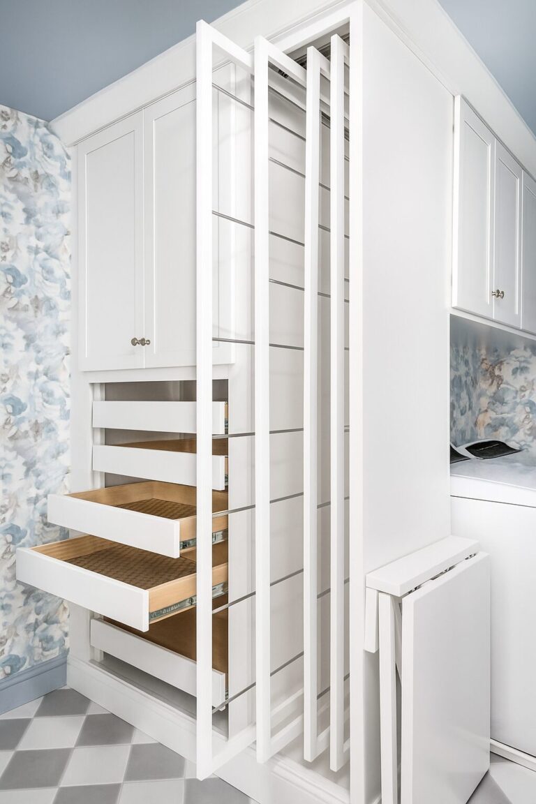 Innovative white laundry room with built-in pull-out drying racks, custom drawer storage, and blue-and-gray floral wallpaper.