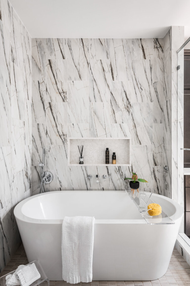 a bathtub and a grey and white shower tiled wall